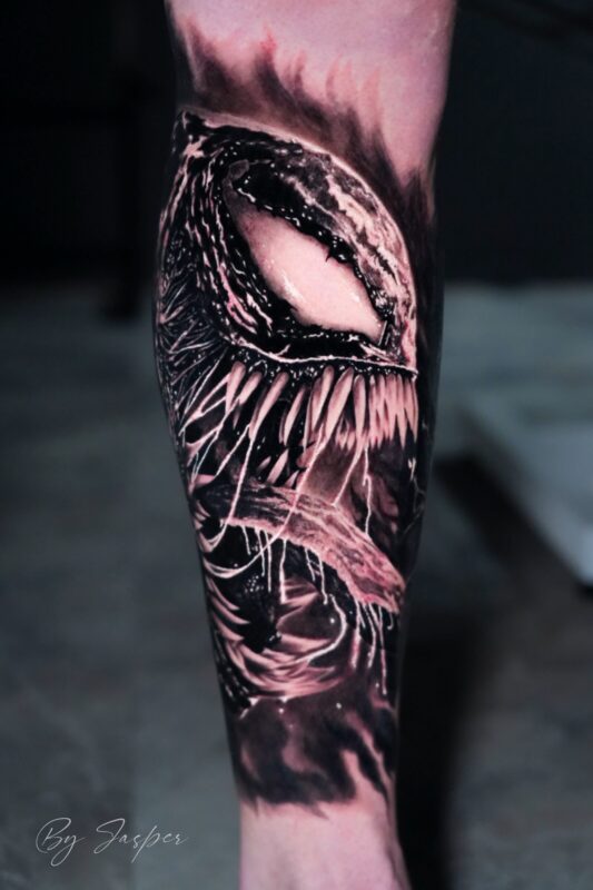 Realistische Venom tattoo op onderbeen, zwart-wit.
