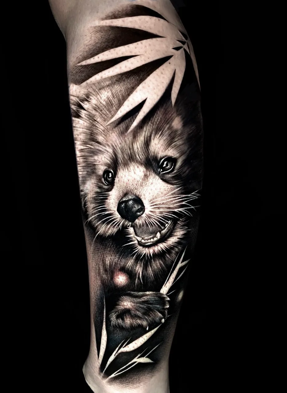 Realistische rode panda tattoo met bamboe bladeren op onderbeen.