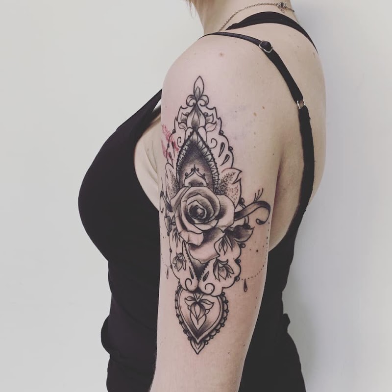 Zwart-wit tattoo van een roos in een sierlijk, decoratief frame op de bovenarm.