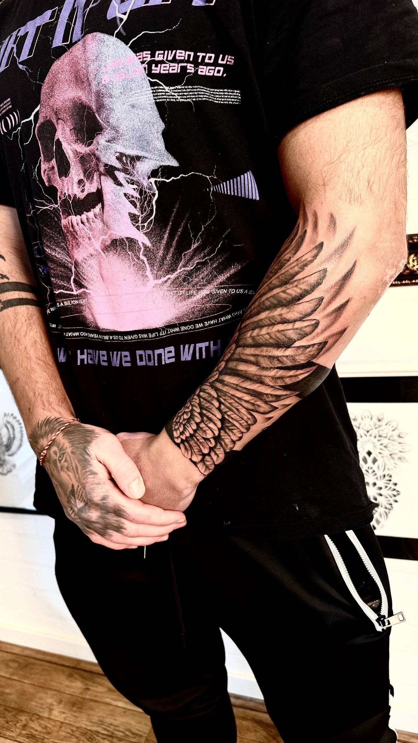 Grote vleugel op onderarm, handtattoo en band op bovenarm.