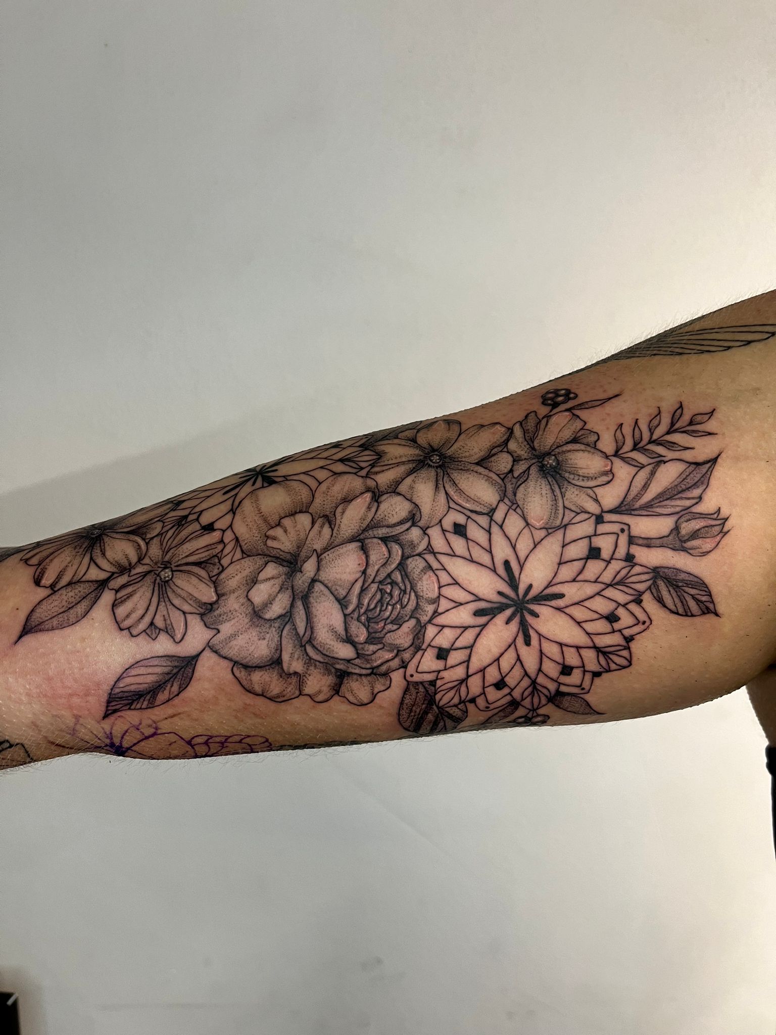 Gedetailleerde blackwork tattoo op de binnenkant van de bovenarm met een roos, bloemen en een mandala.