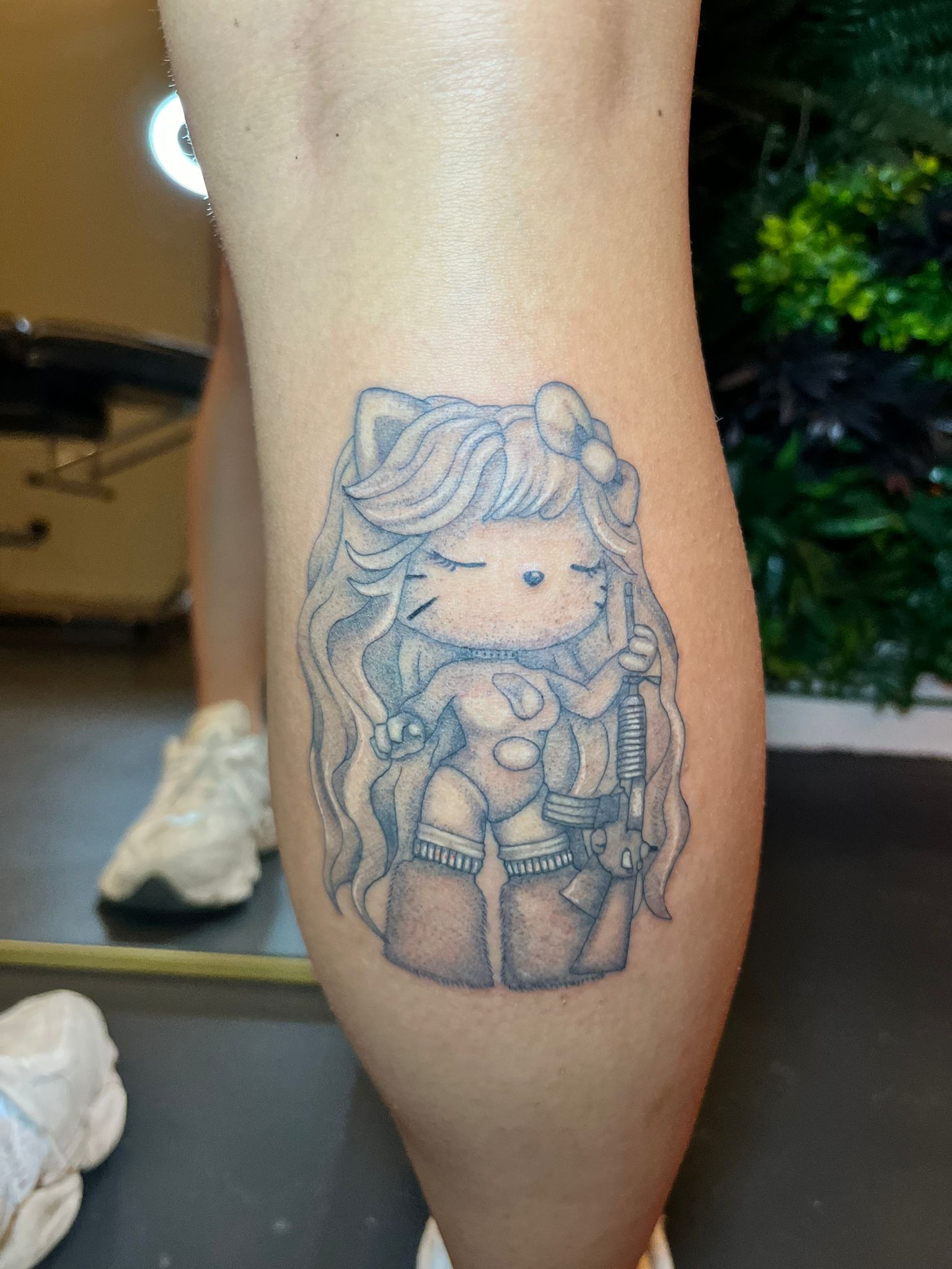 Fineline tattoo van Hello Kitty met lang haar, bikini, laarzen en een geweer.