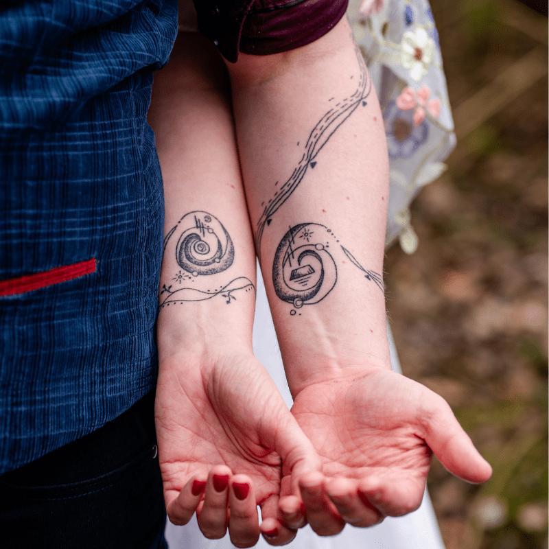Twee bijpassende fineline tattoos van spiraalvormige melkwegstelsels op onderarmen.