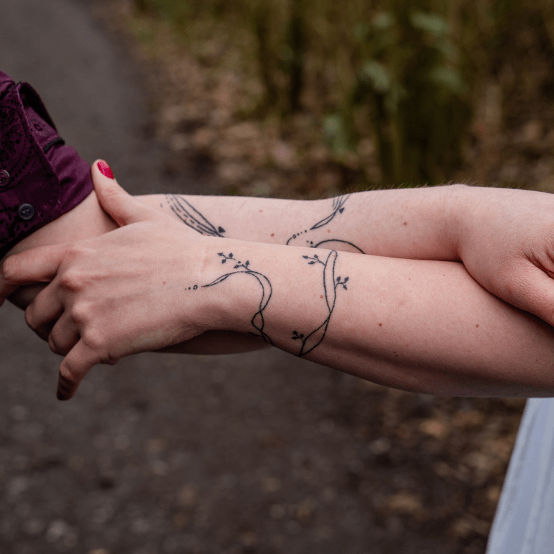 Twee bijpassende fineline takken met bladeren op onderarmen.