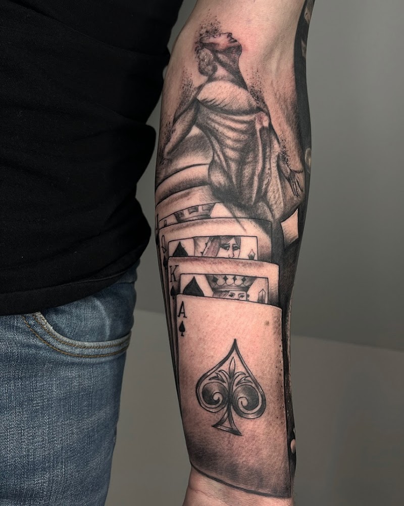 Zwart-wit tattoo van speelkaarten en een figuur dat oplost in deeltjes.