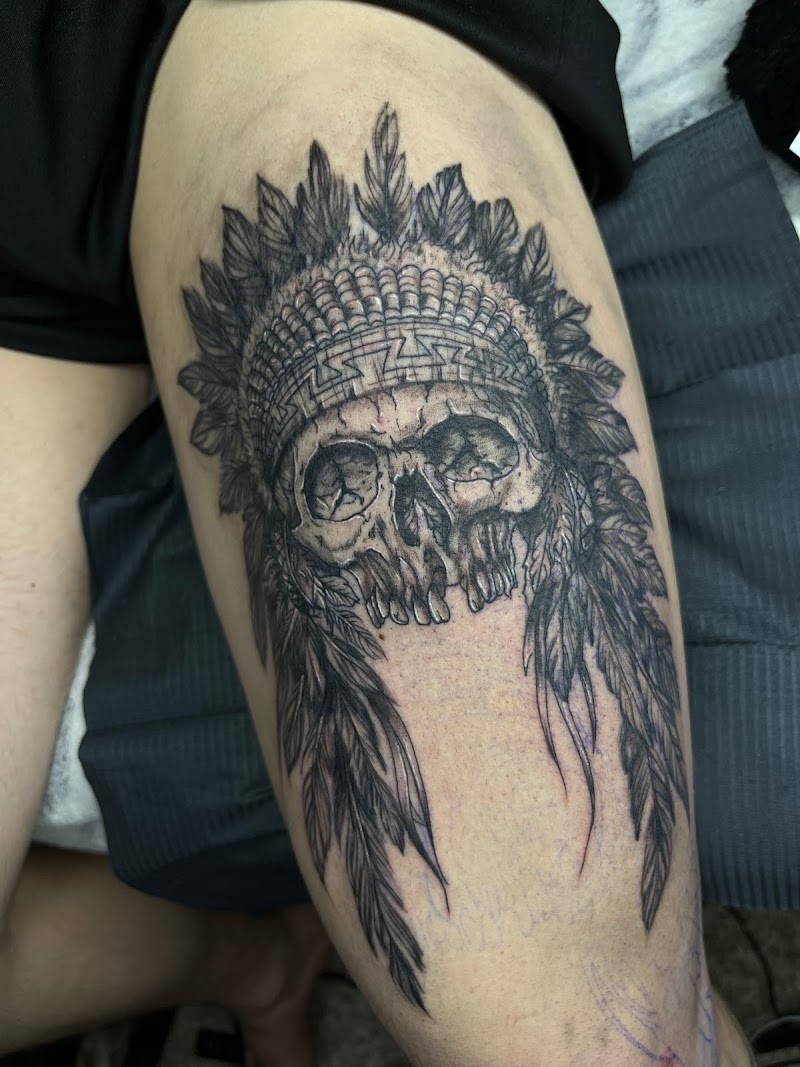 Zwart-wit tattoo van een schedel met een indianentooi op het bovenbeen.
