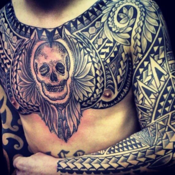 Grote tribal tattoo op borst en arm met een centrale schedel.