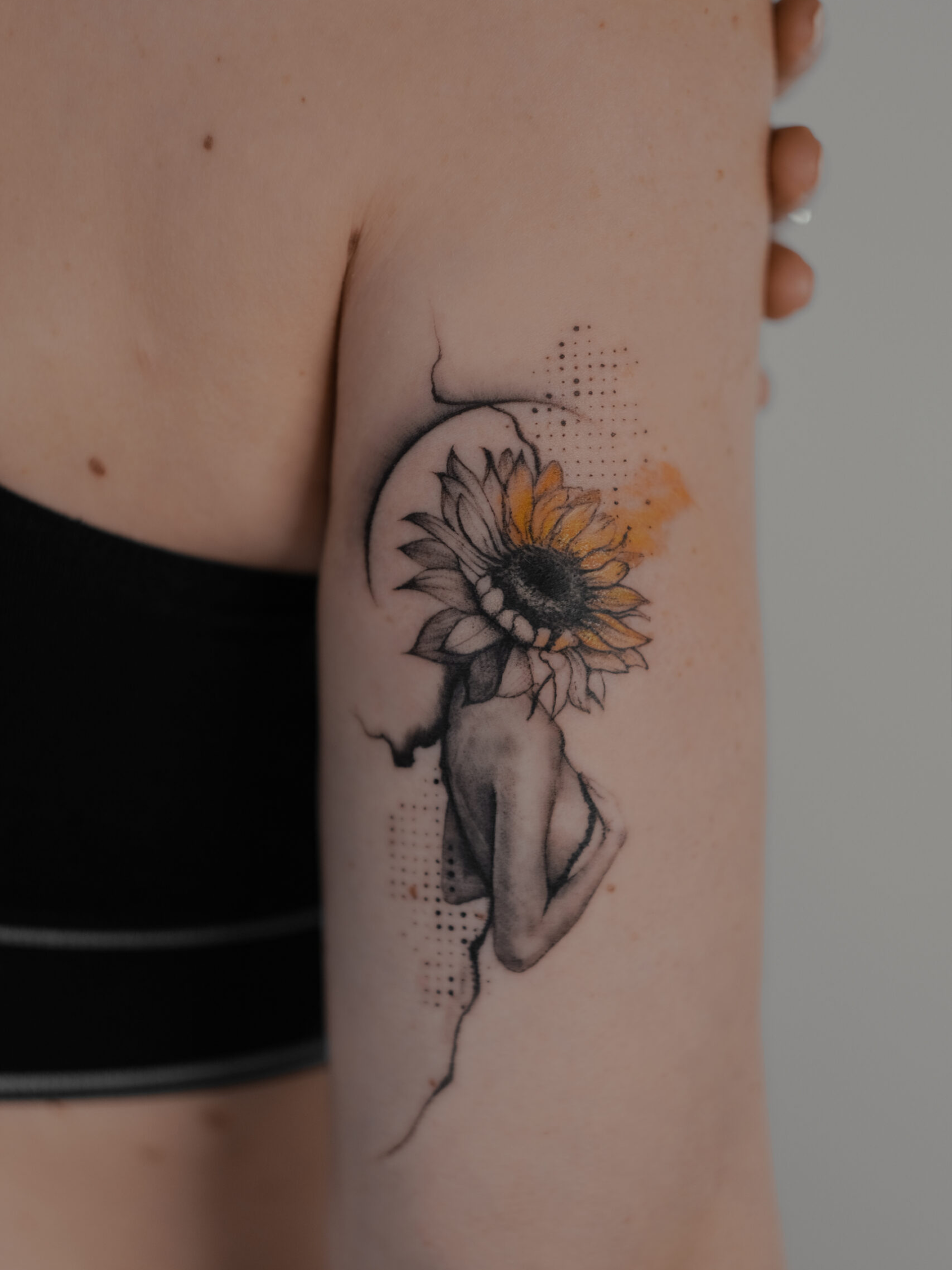Surrealistische tattoo van vrouw met zonnebloemhoofd op bovenarm.