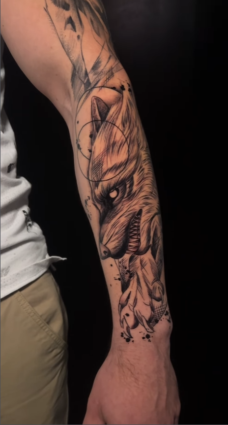 Zwart-wit wolf tattoo met geometrische lijnen en spetters op onderarm.