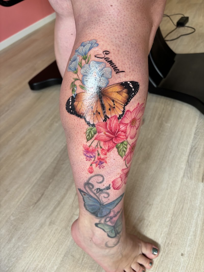 Kleurrijke monarchvlinder met bloemen en de naam 'Samuel' op het onderbeen.