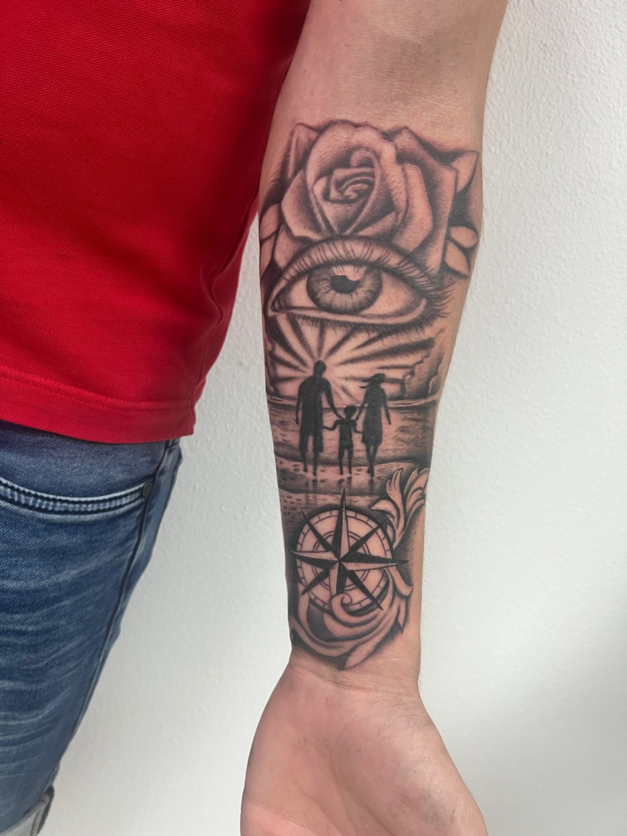 Zwart-wit onderarm tattoo met roos, oog, gezin op strand en kompas.