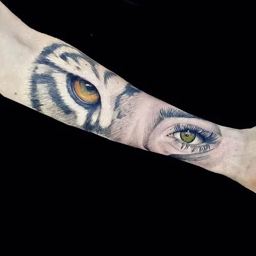 Realistische tattoo van een tijgeroog dat overgaat in een mensenoog op de onderarm.