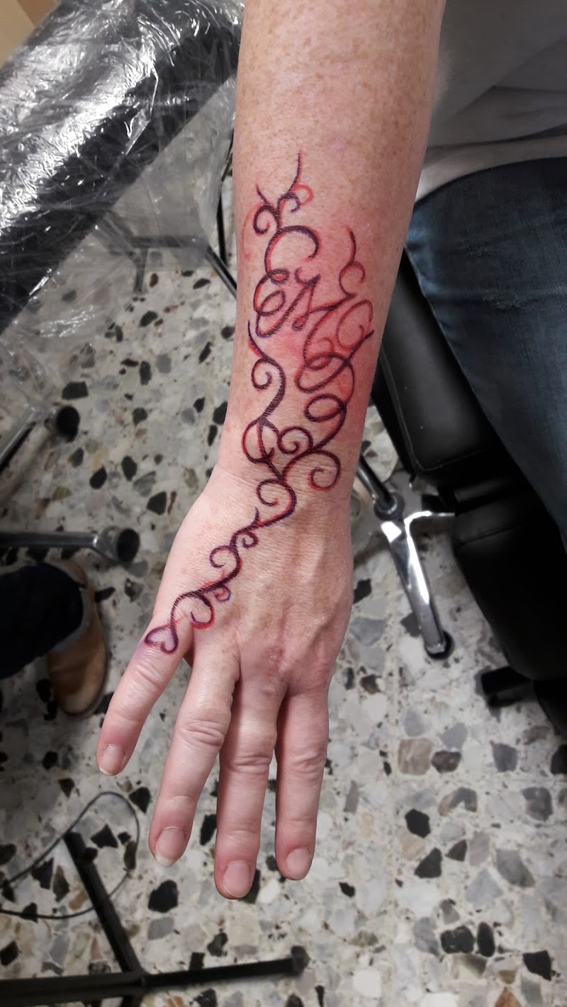 Sierlijke abstracte krullen tattoo in rood/paars op onderarm en hand.