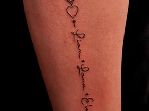Fineline tattoo met namen Liam, Lana, Ela en hartjes op onderarm.