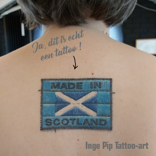 Realistische 'MADE IN SCOTLAND' kledinglabel tattoo op de bovenrug.