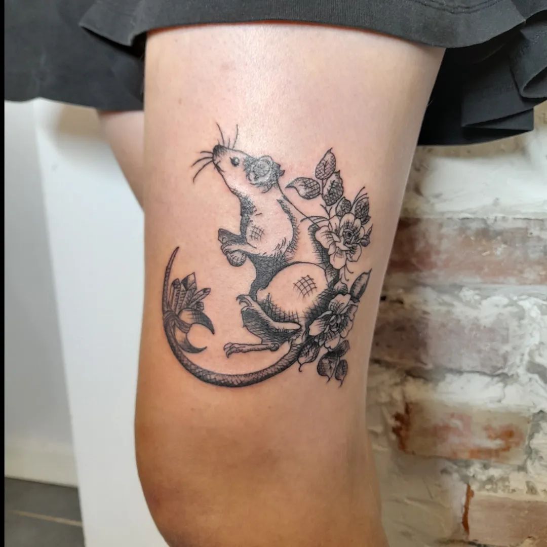 Gedetailleerde gravure-stijl tattoo van een rat met bloemen op het bovenbeen.