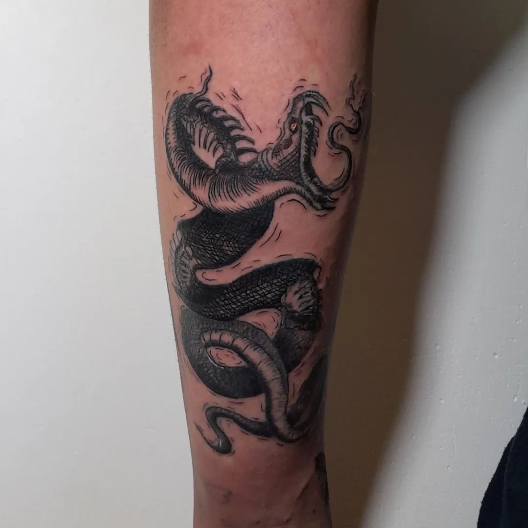 Zwart-wit illustratieve draak tattoo op onderbeen.