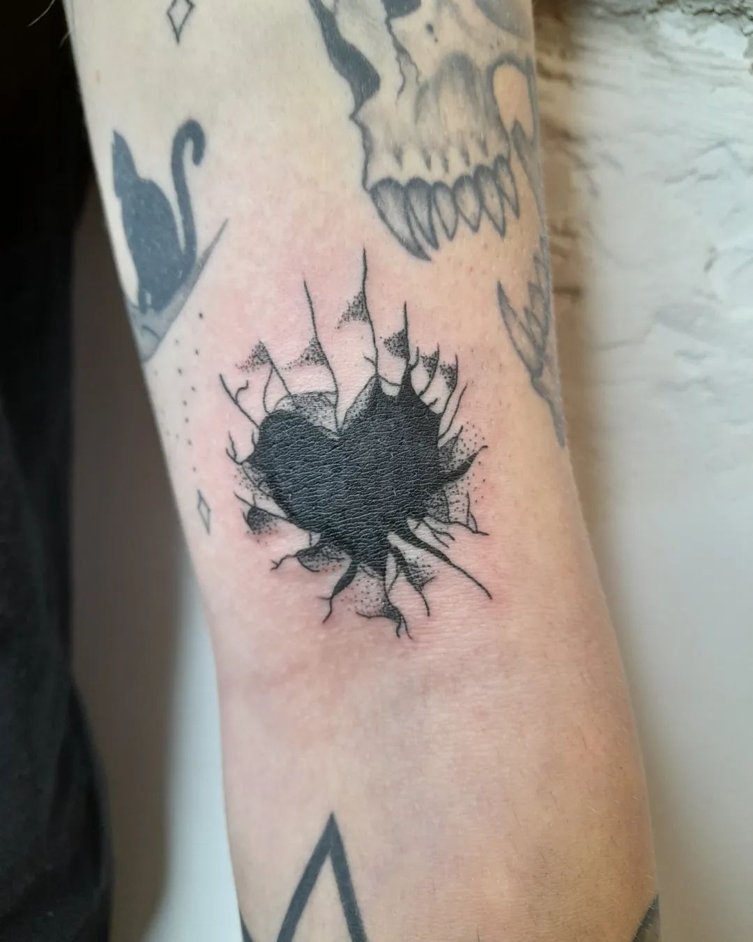 Zwart gebroken hart tattoo met barsten op de achterkant van de bovenarm.