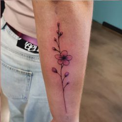 Fijne lijn bloementak tattoo met roze/paarse tinten op onderarm.