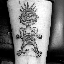 Zwart-wit tattoo van een eenogig monster met een mond op de buik.