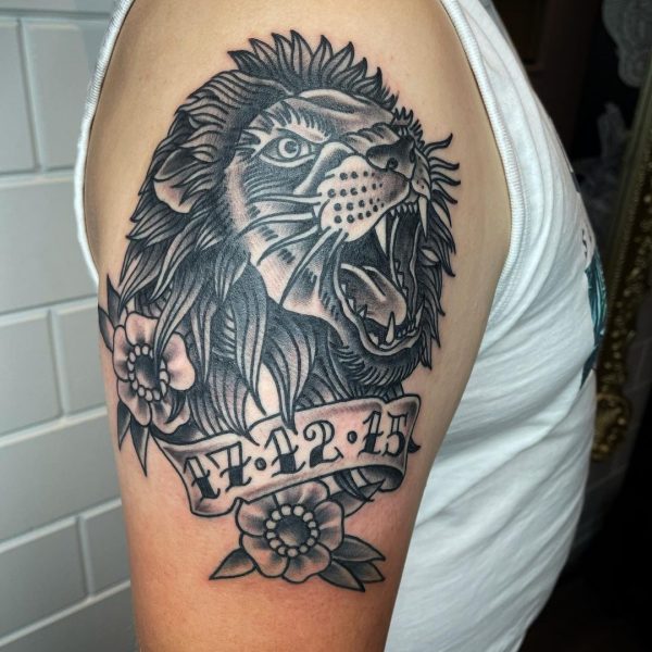 Traditionele leeuwenkop met bloemen en datum banner op bovenarm.