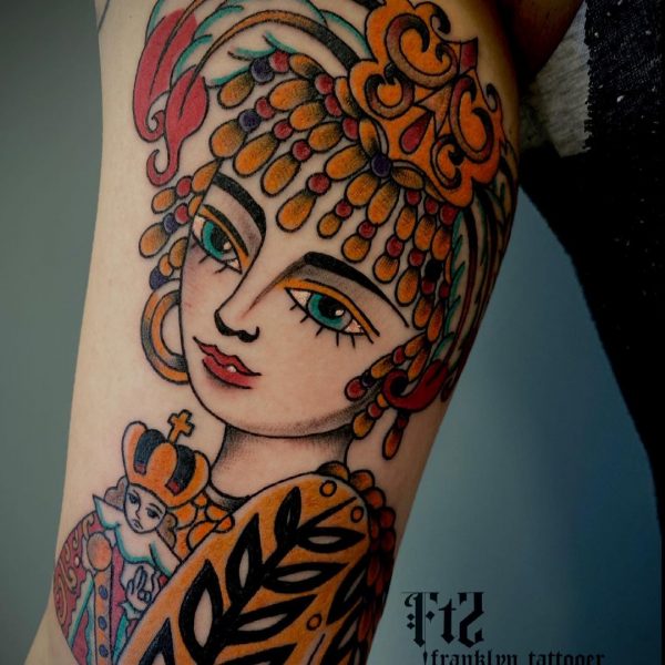 Kleurrijke traditionele tattoo van een vrouw met hoofdtooi en klein gekroond figuur.