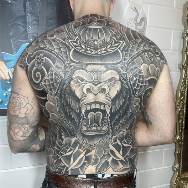 Grote zwart-wit rugtattoo van een gorilla in samoerai-uitrusting met bloemen.
