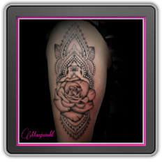 Zwart-wit tattoo van een roos in een ornamenteel mandala patroon op de bovenarm.