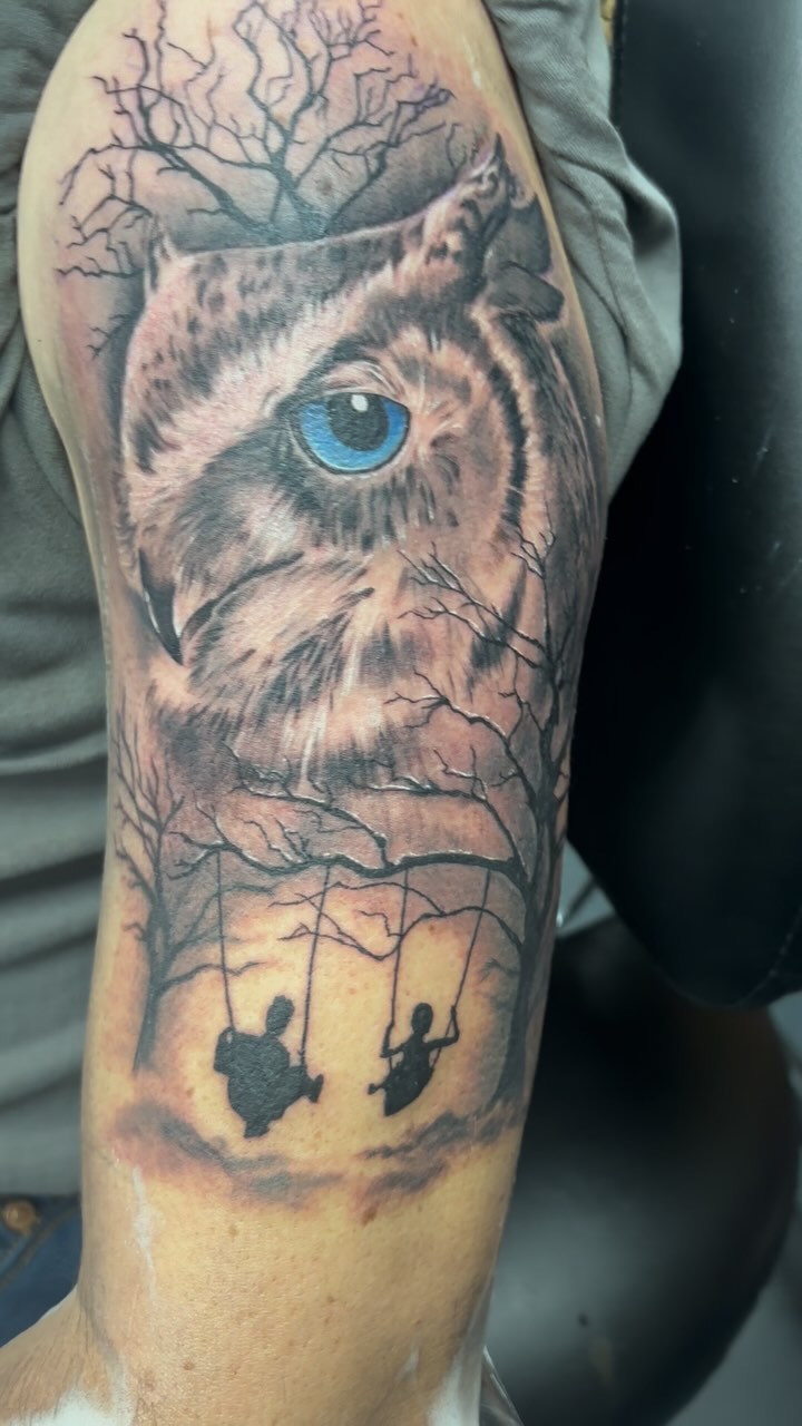 Realistische uil met felblauw oog en silhouetten op schommels op bovenarm.