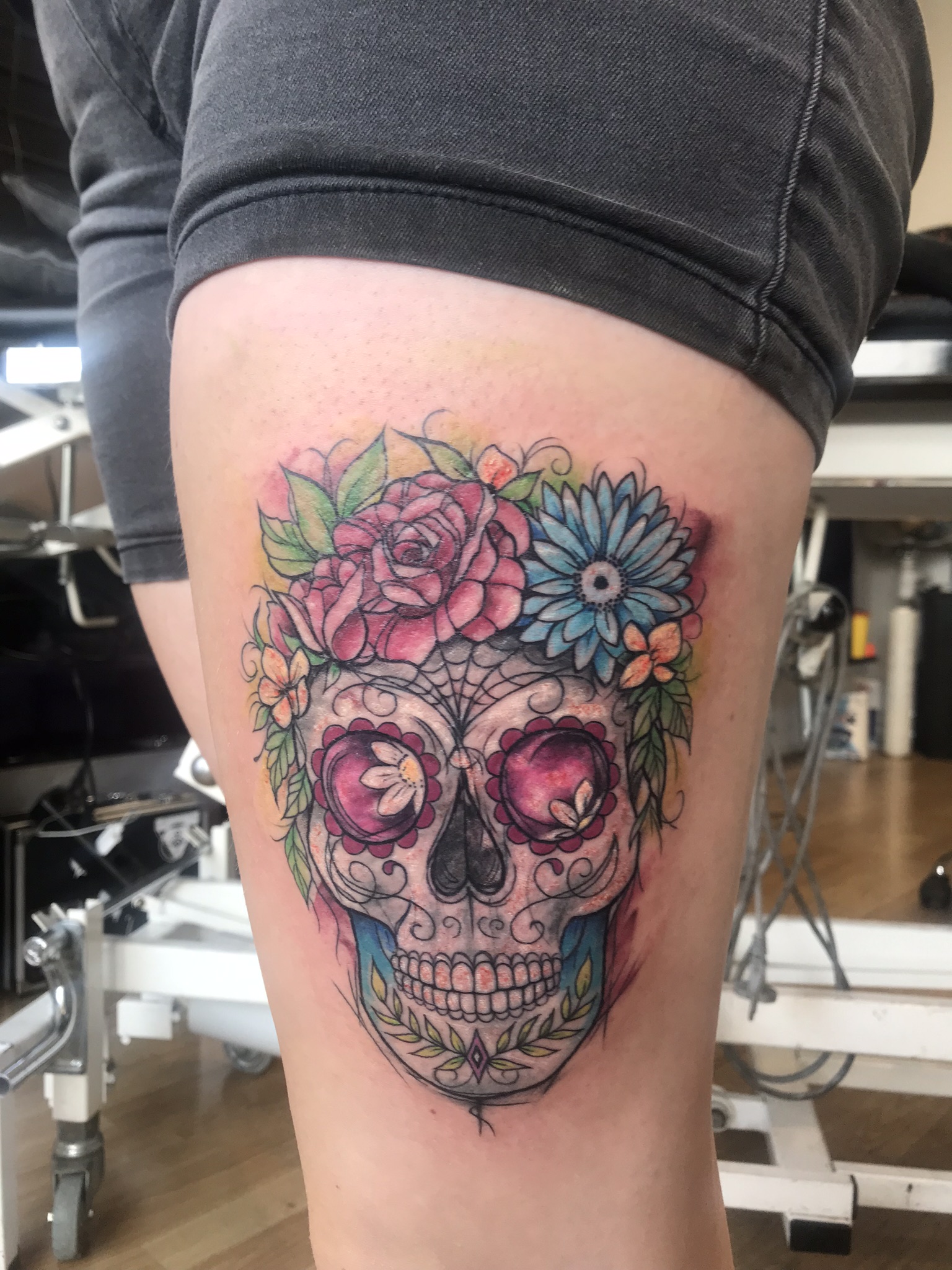 Kleurrijke sugar skull met bloemen op het bovenbeen.