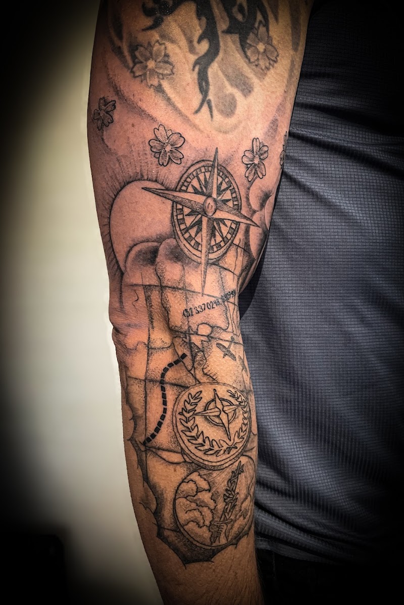 Zwart-wit tattoo van kompas, landkaart en kersenbloesems op arm.