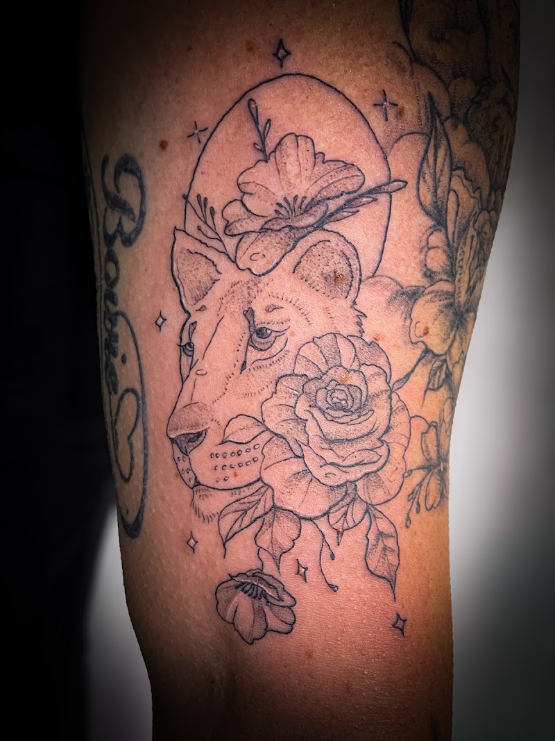 Fineline leeuwin met bloemen en sterren op bovenarm.
