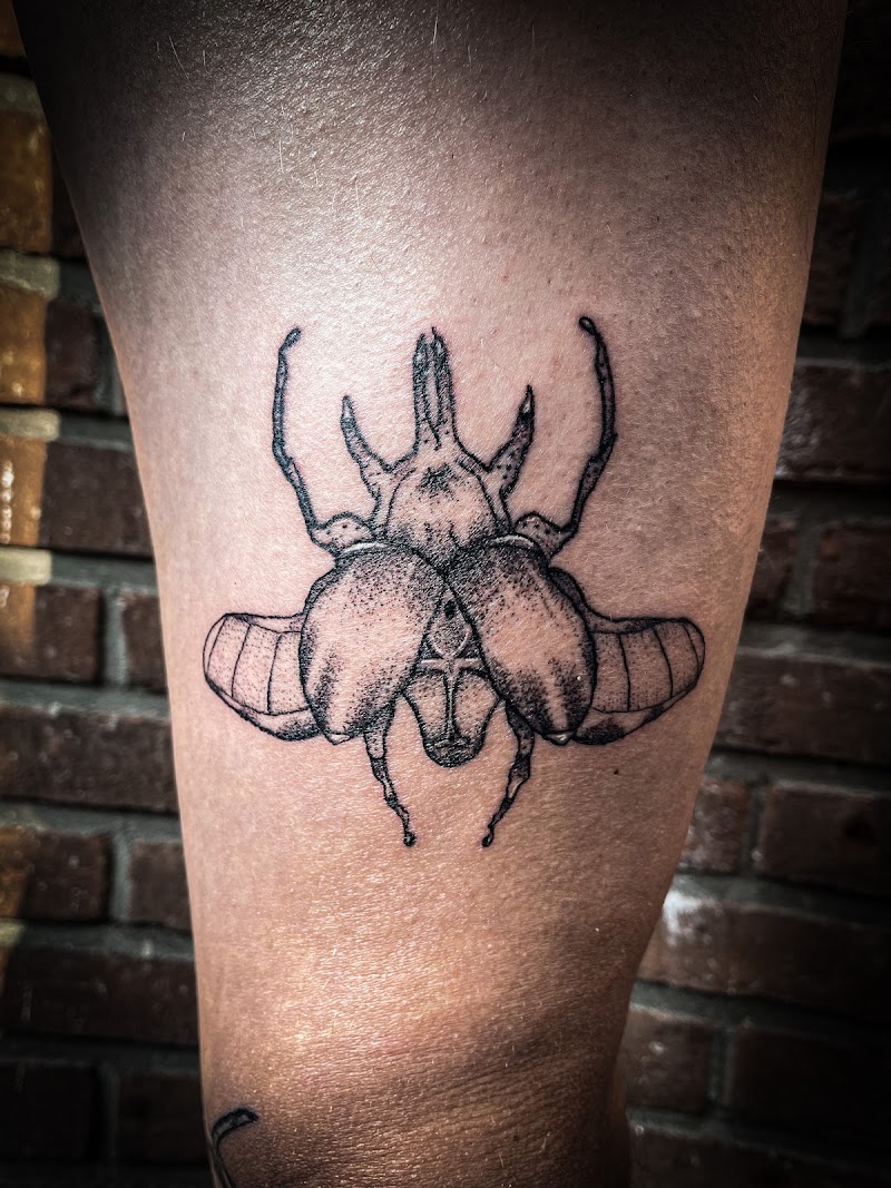 Gedetailleerde blackwork kever tattoo op het bovenbeen.