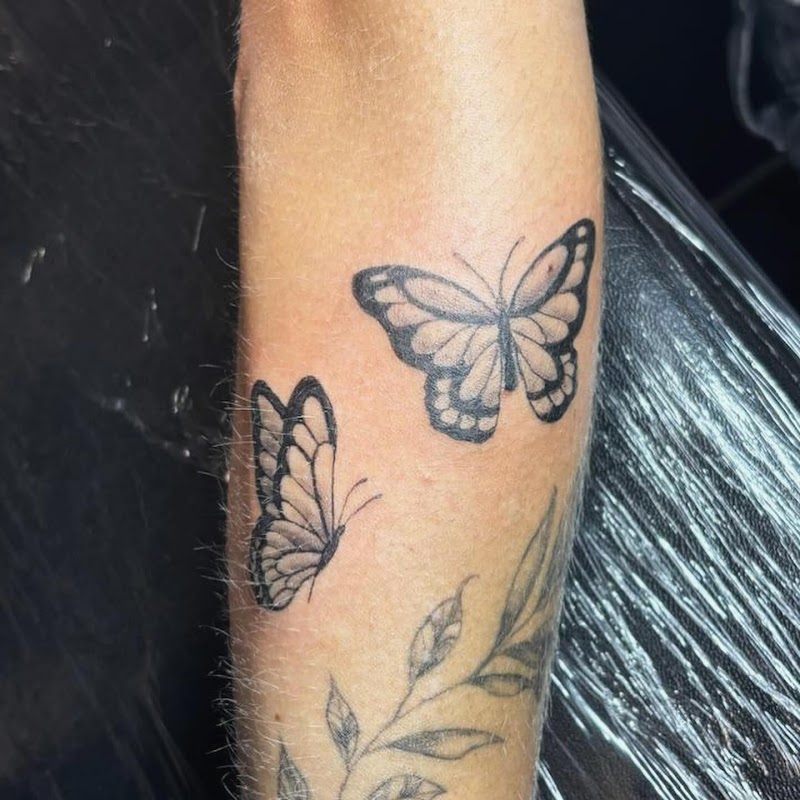 Twee fineline vlinders en een tak met bladeren op de onderarm.