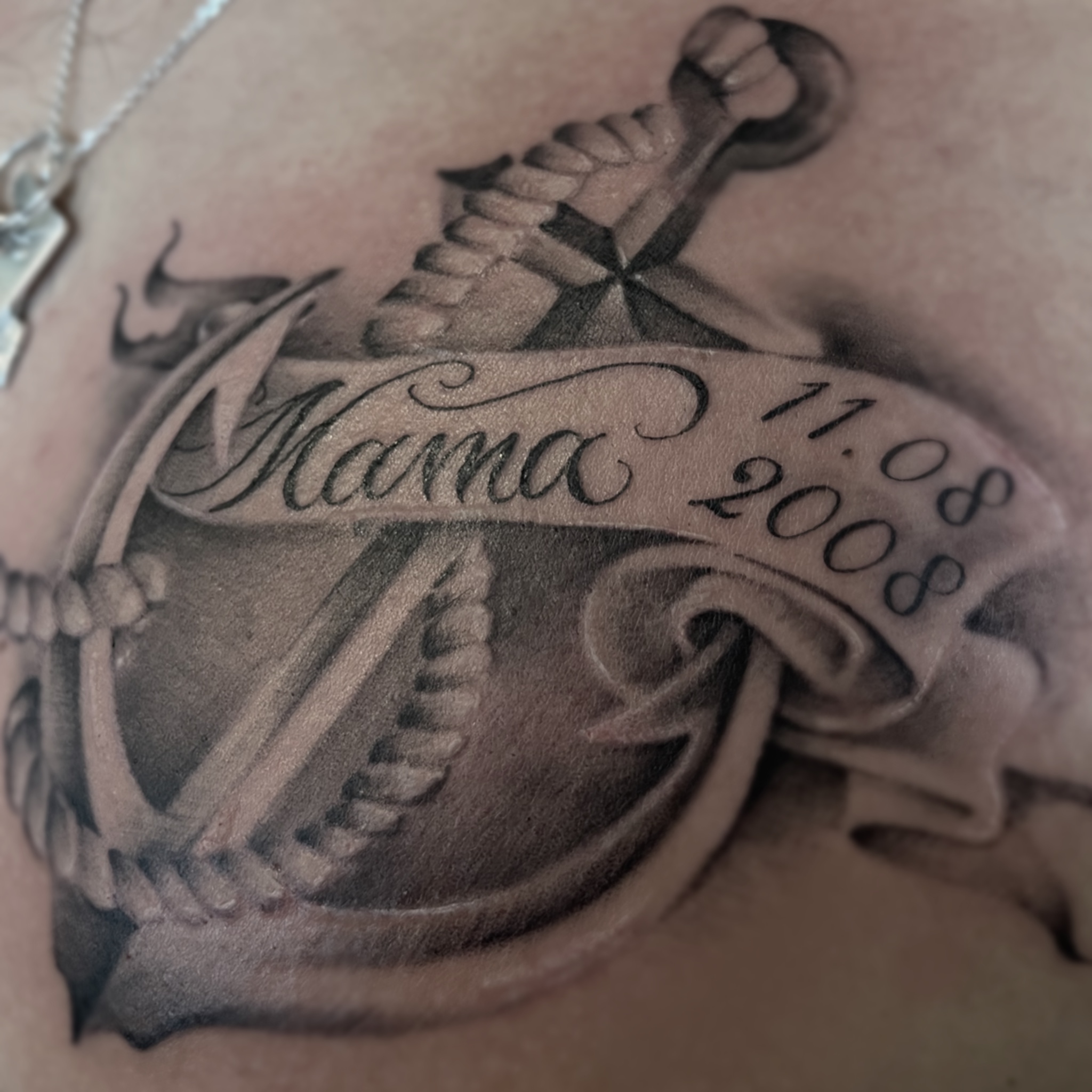 Zwart-wit anker tattoo met 'Mama' en '11.08 2008' op een spandoek.