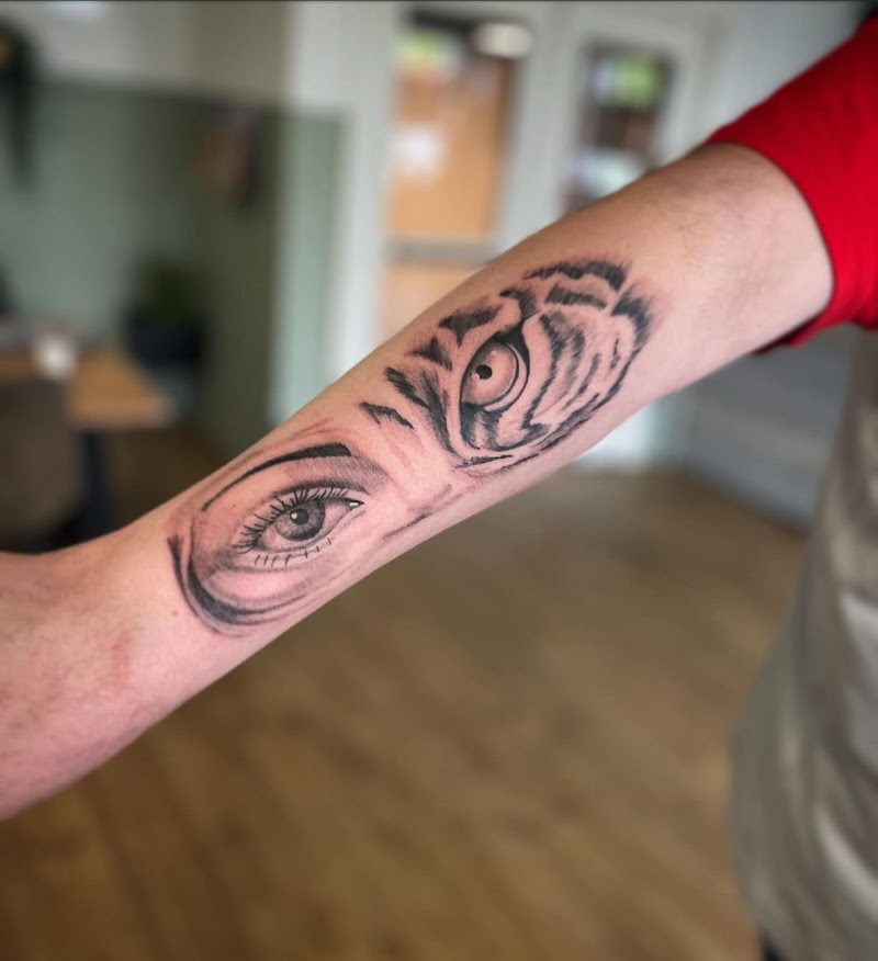 Realistische tattoo van een mensenoog en een tijgeroog op de onderarm.