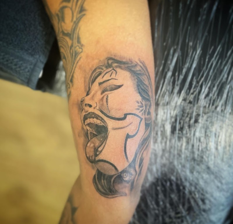 Black & grey tattoo van een schreeuwend vrouwengezicht met een masker op de bovenarm.