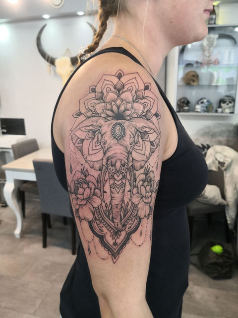 Grote olifant met mandala en bloemen op bovenarm in blackwork stijl.