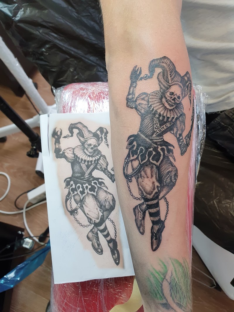 Gedetailleerde zwart-wit tattoo van een dansend skelet in narrenpak op de onderarm.