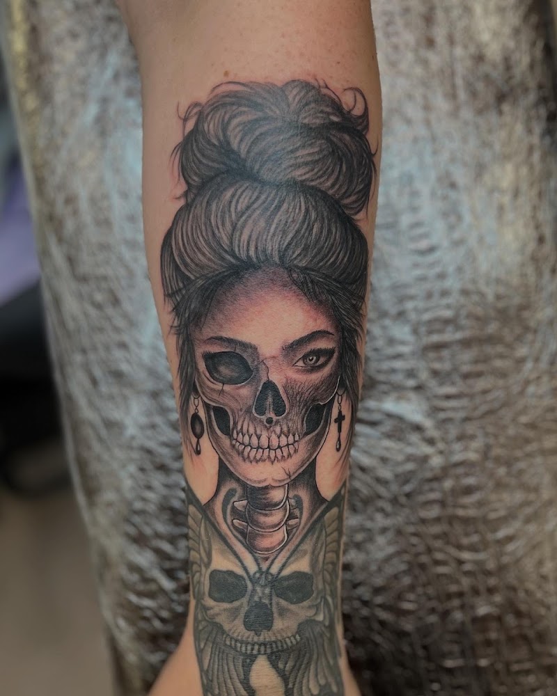 Zwart-wit tattoo van een vrouw met half schedelgezicht en knot op de onderarm.