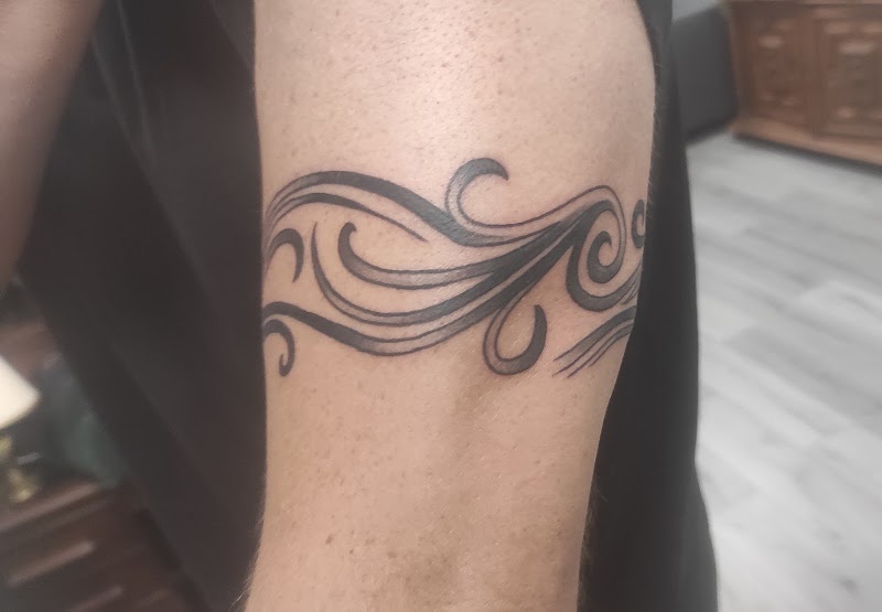 Zwart-witte tribal band tattoo met golvende lijnen op de bovenarm.