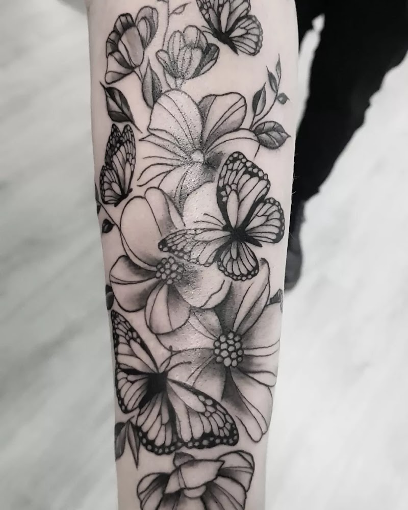 Zwart-wit tattoo van vlinders en bloemen op de onderarm.