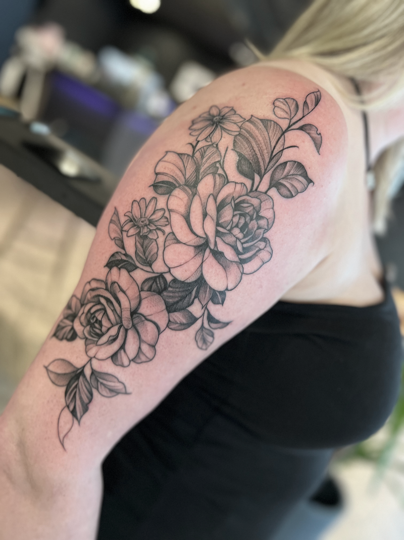 Grote fineline bloemen tattoo met rozen en bladeren op bovenarm.