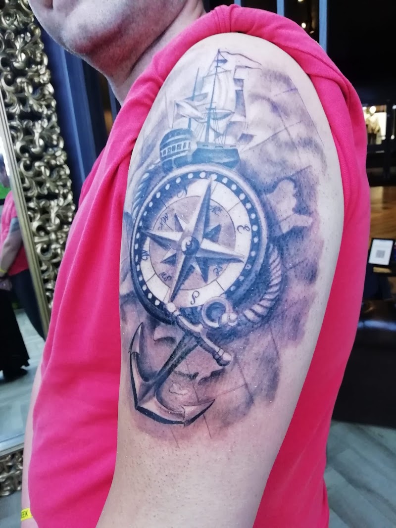 Zwart-wit tattoo van een kompas, anker en zeilschip op de bovenarm.
