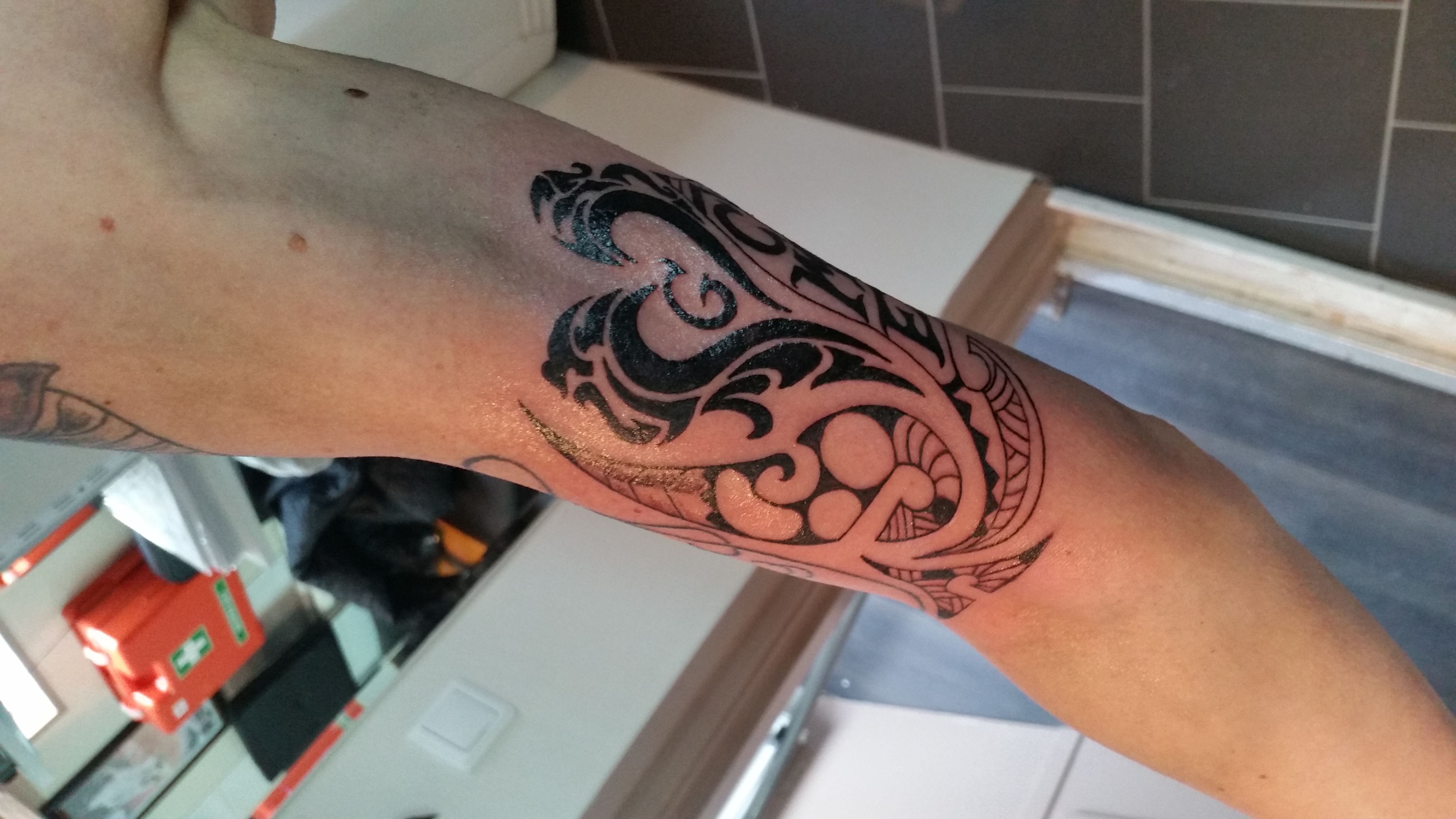 Zwarte tribal tattoo op bovenarm met abstracte vormen.