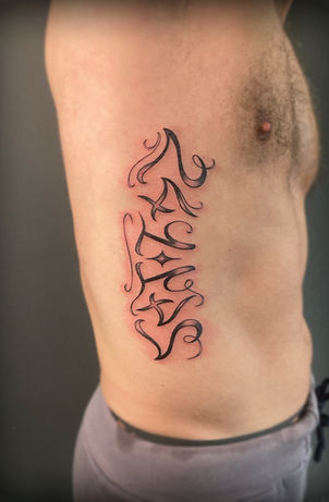 Verticale teksttattoo in sierlijk script op de ribben.