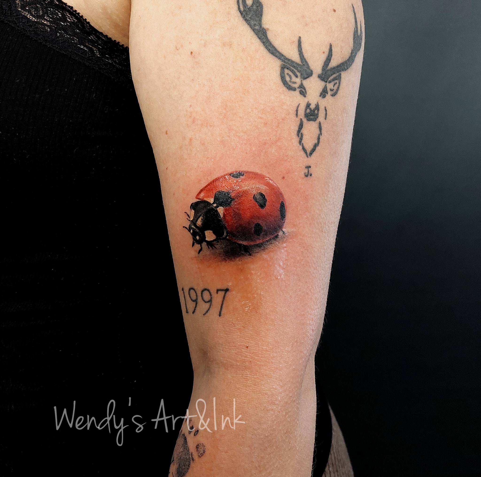 Realistisch lieveheersbeestje, fineline hertenkop en jaartal 1997 op bovenarm.