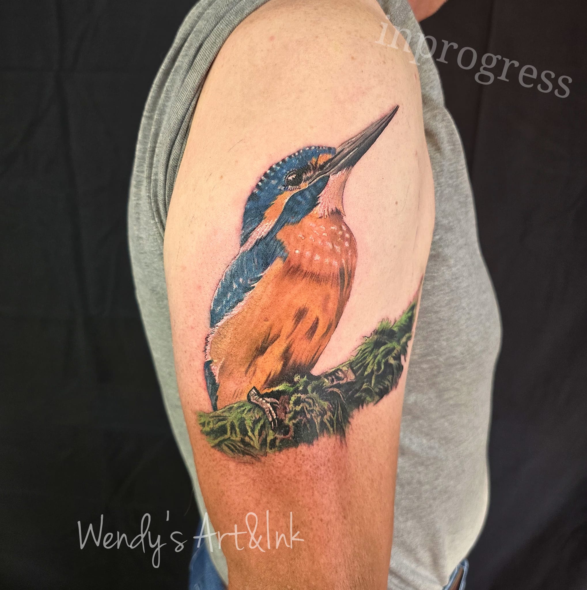 Realistische ijsvogel op een bemoste tak op de bovenarm.