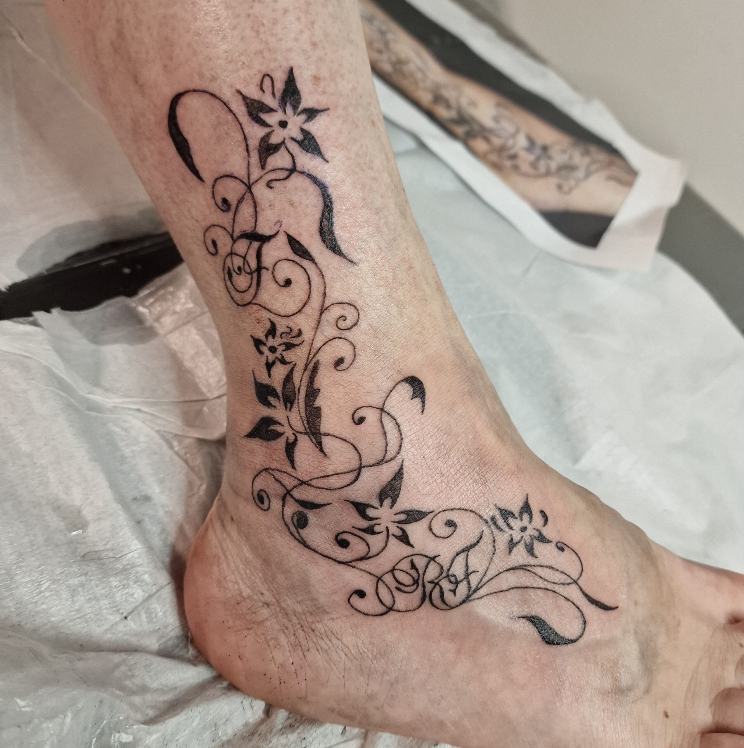 Zwart-witte bloemen en krullen tattoo op enkel en voet.