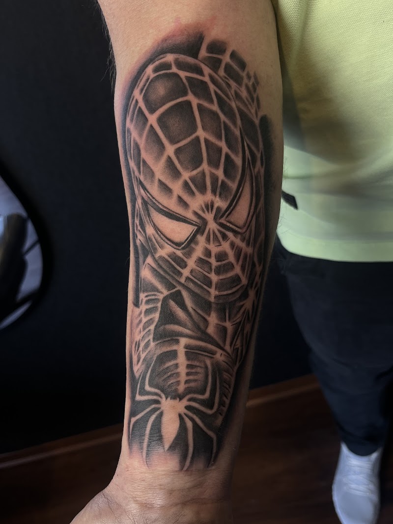 Zwart-wit Spider-Man masker en logo tattoo op onderarm.